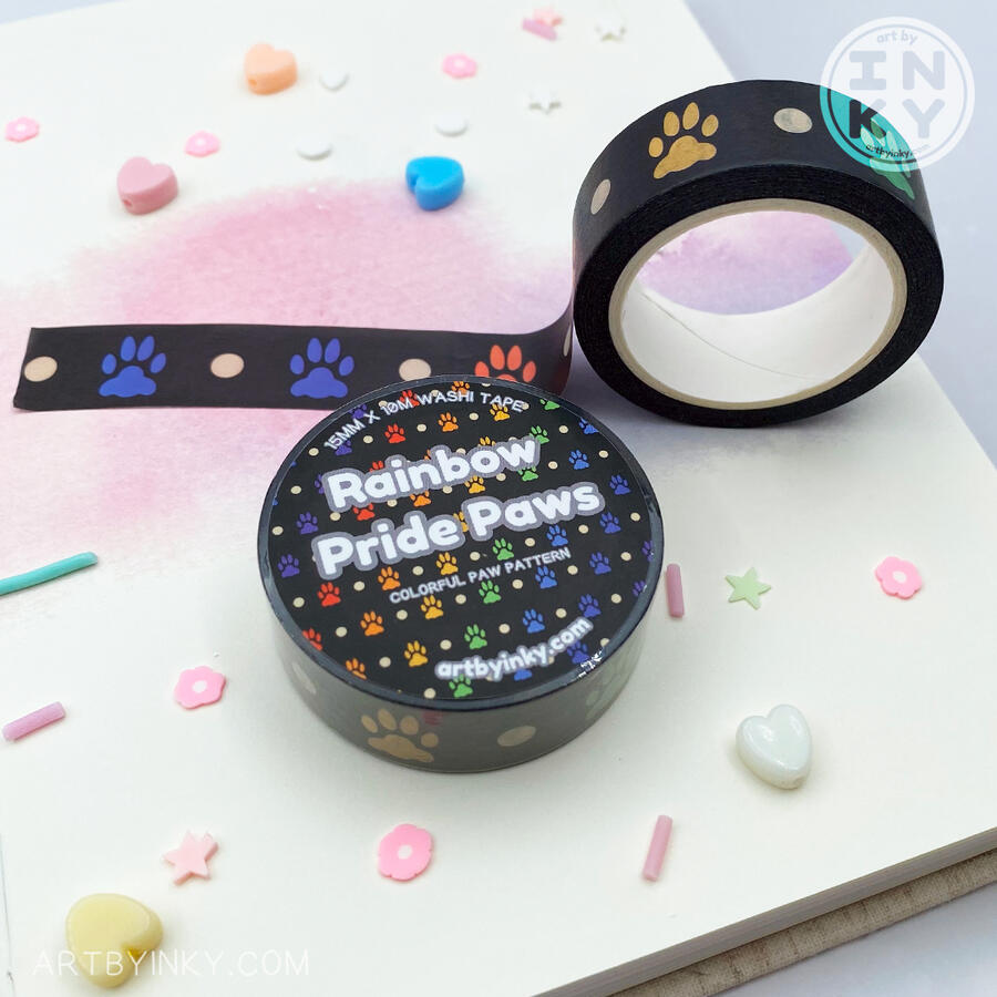 Opened and unopened rainbow pride paws pattern washi tape rolls laid out on a hardcover journal.