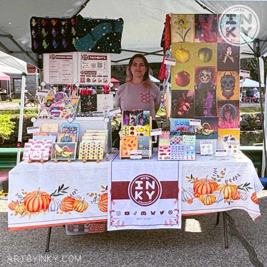 Full front view of the booth layout at an outdoor market surrounded by products like art prints, stickers, washi tape tote bags, journals, bookmarks, pins, greeting cards, and coin purses.