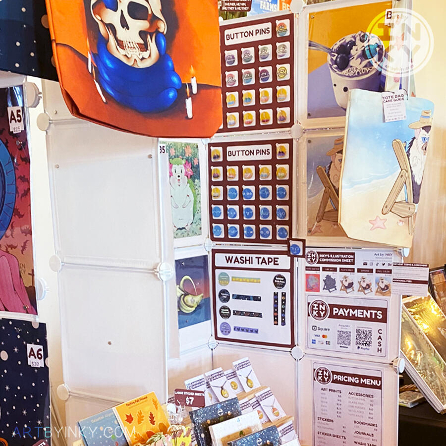 Side view of the booth layout at an anime convention showing pins and art prints.