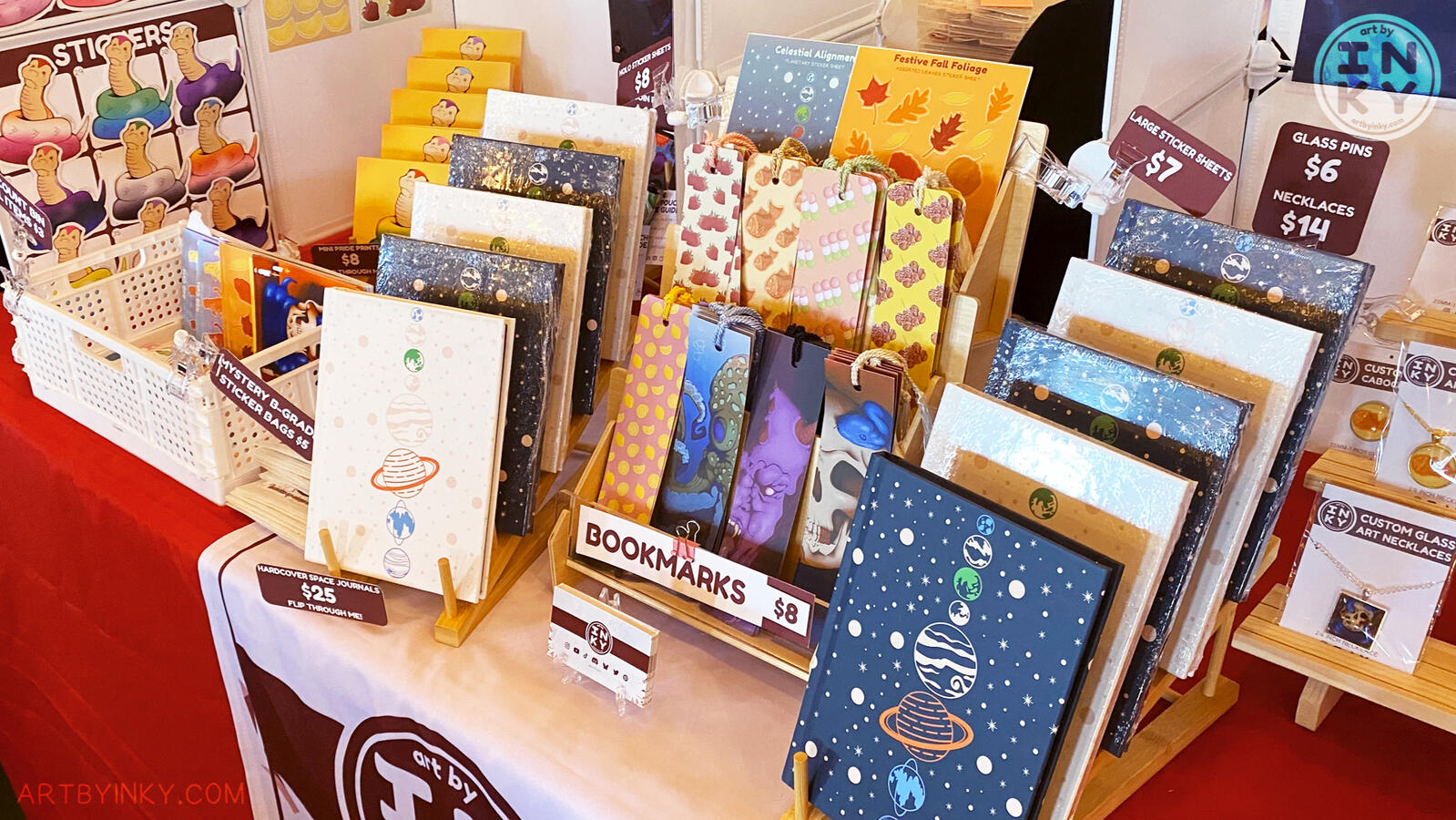 Table Layout Top Down Side view of the booth layout at an anime convention showing products like art prints, stickers, washi tape, tote bags, journals, bookmarks, pins, jewelry, and coin purses.